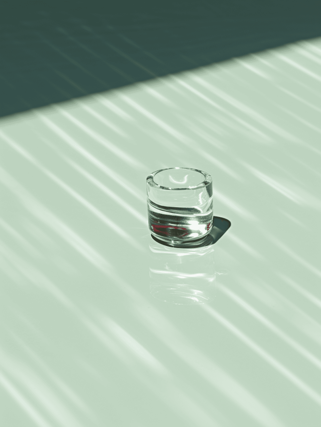 A single glass on a pale green surface striped with light